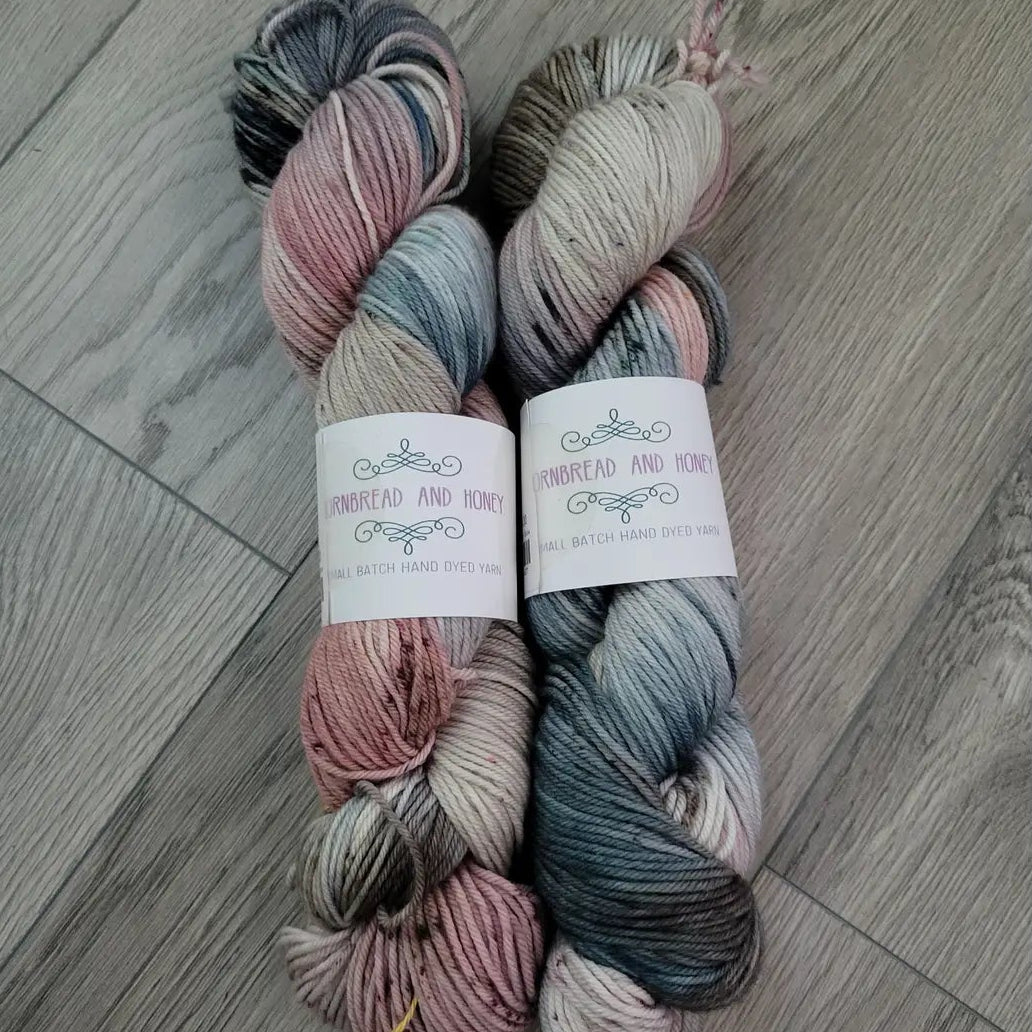 Two skeins of multicolored yarn on a wooden floor with labels.