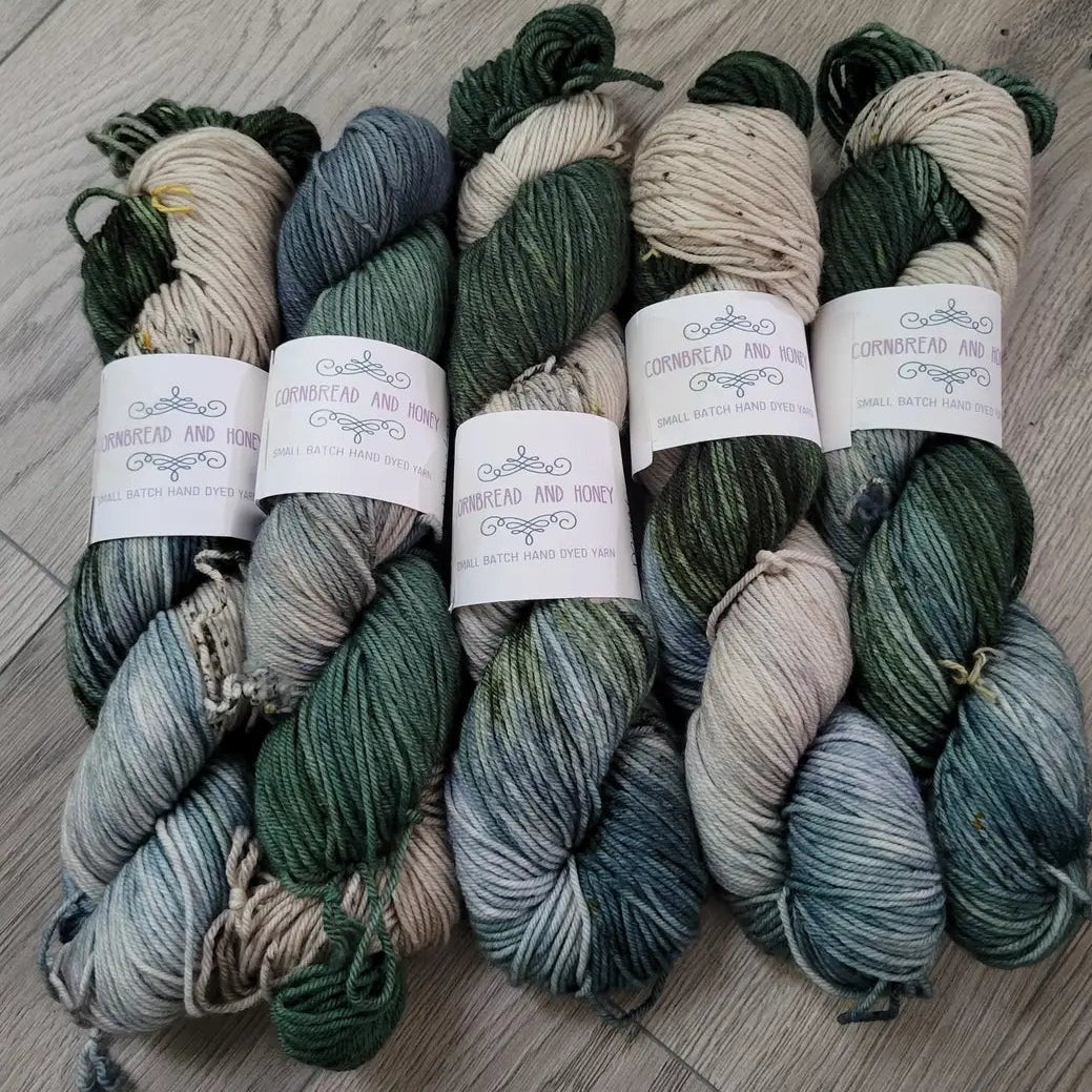 Five skeins of green and beige yarn on a wooden floor